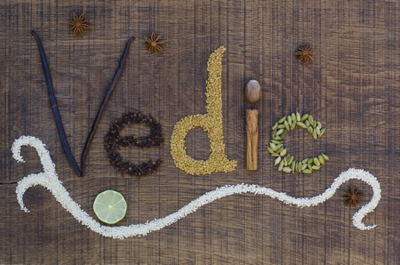 The word Vedic spelled out in ayurveda spices and seeds on a wooden countertop